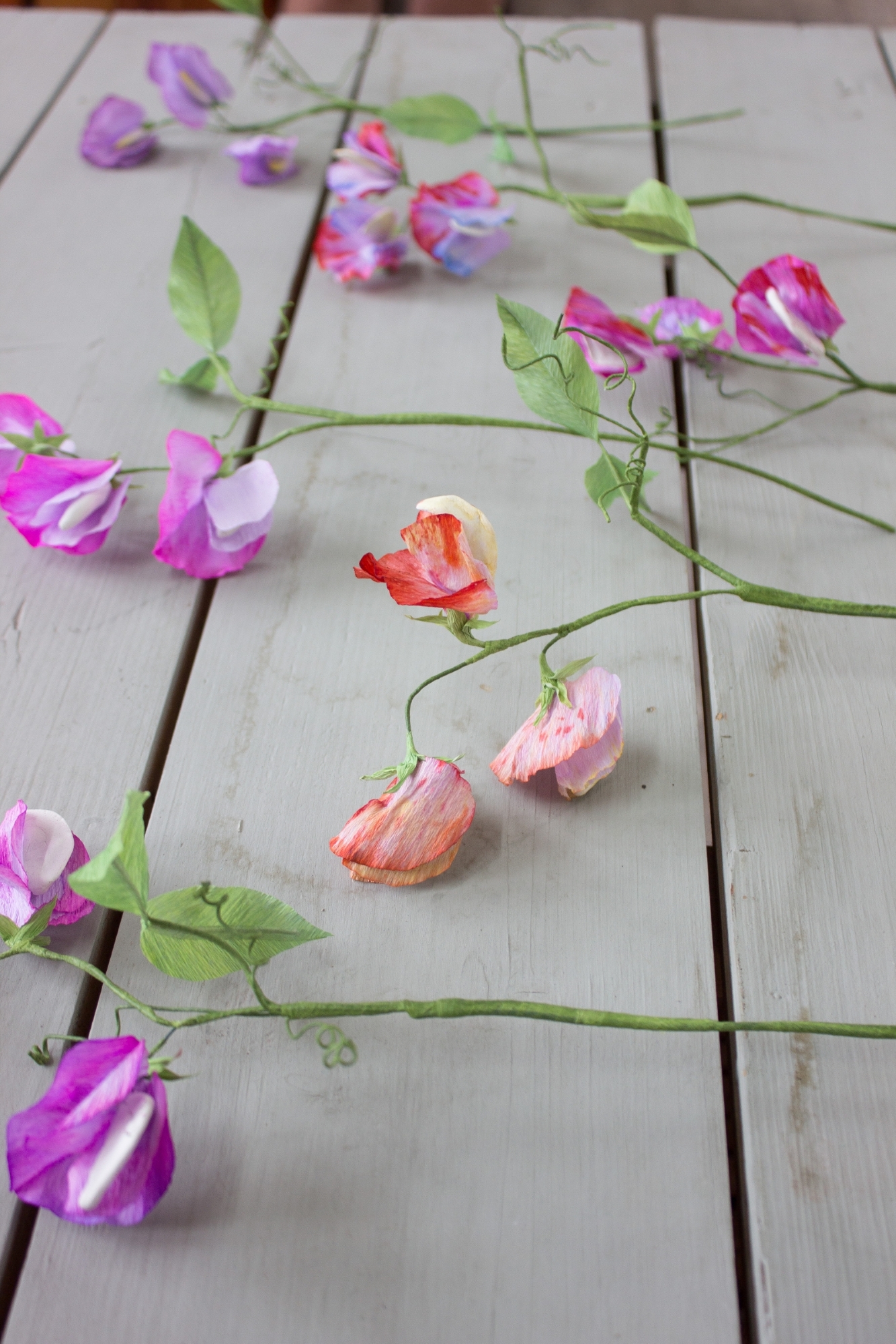 handmade paper sweet peas in pink orange and blue, laid on light grey wood